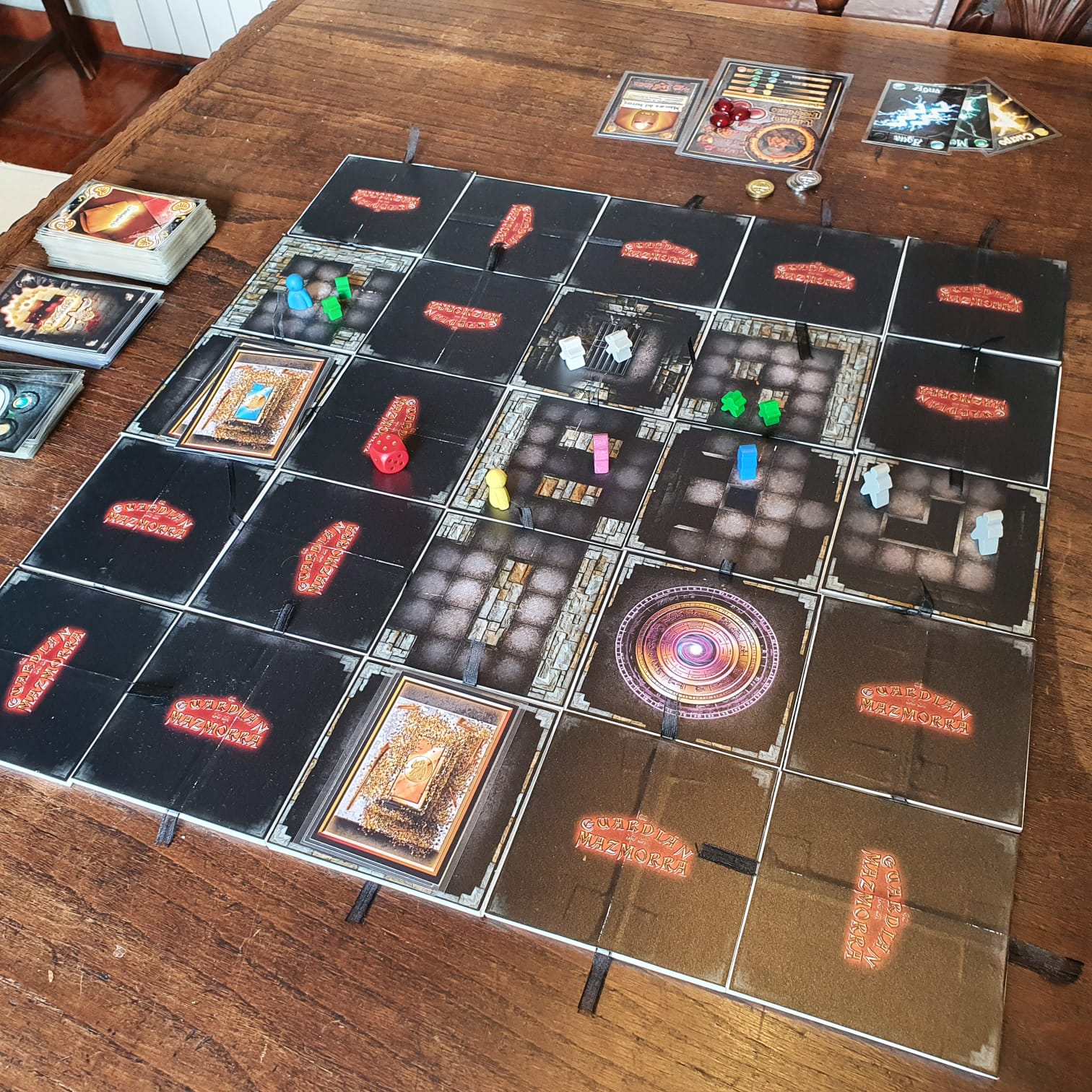 A handmade dungeon board game laid out on a wooden table, with modular rooms, cards, dice and coloured playing pieces.